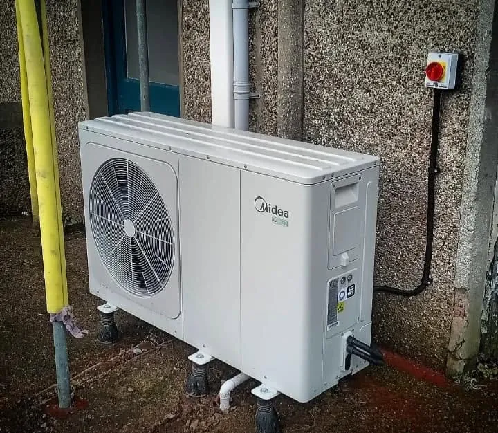 Midea outdoor air conditioning unit on feet beside a pebbledash wall with isolator switch