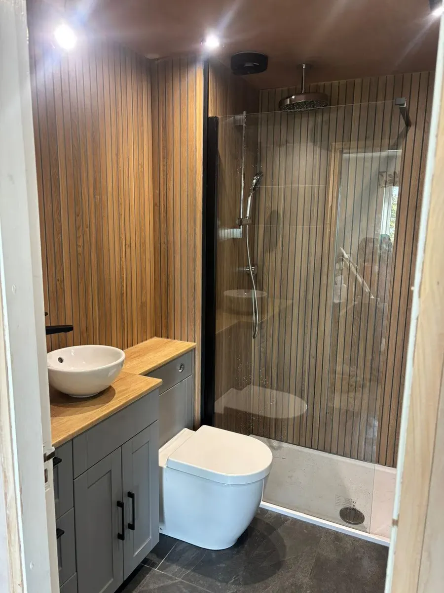 After: finished shower room with wood slat panelling, glass screen, rain shower, grey vanity and dark floor tiles