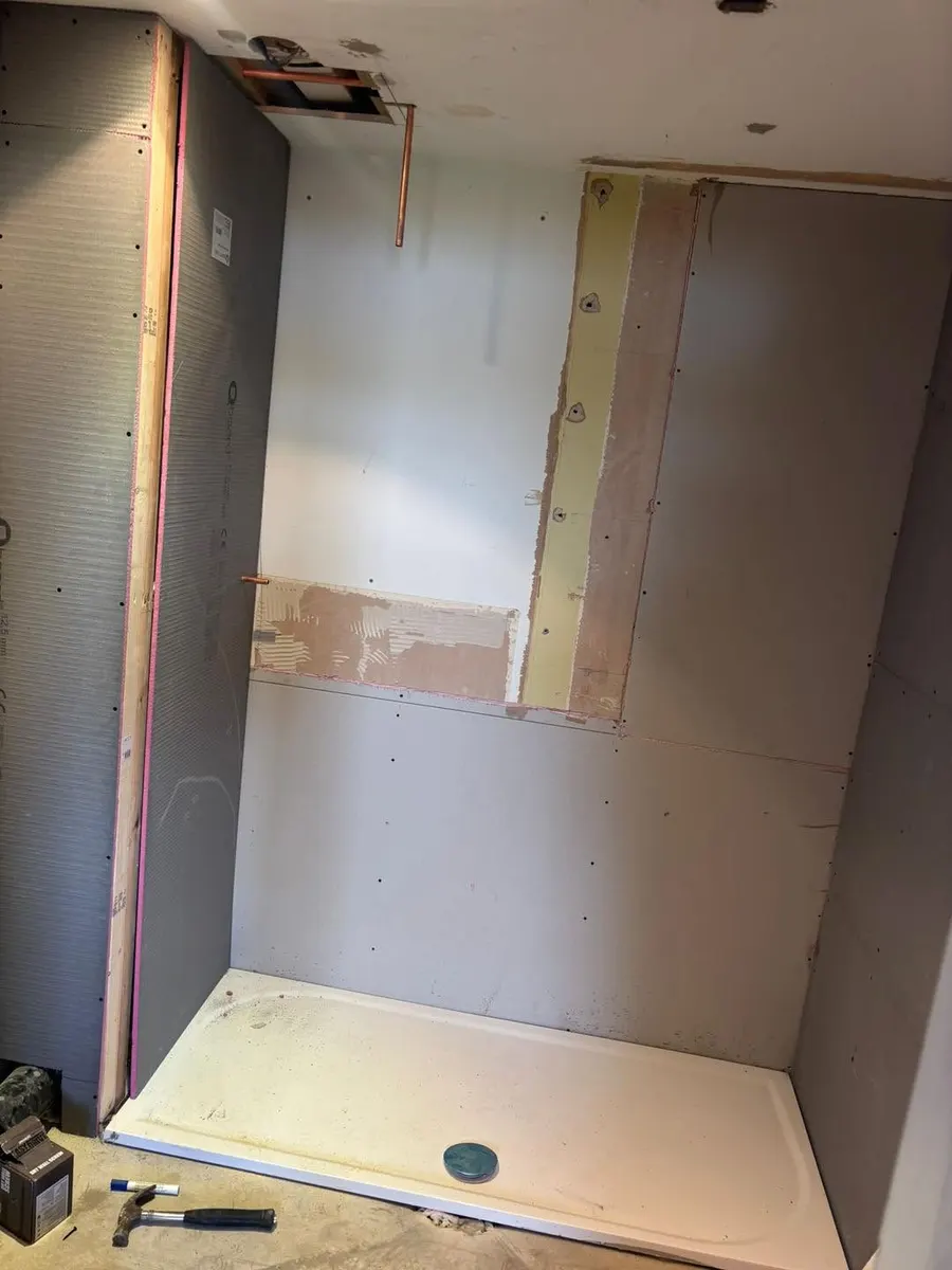Before: stripped shower room with bare boards, exposed copper pipes and the shower tray in place