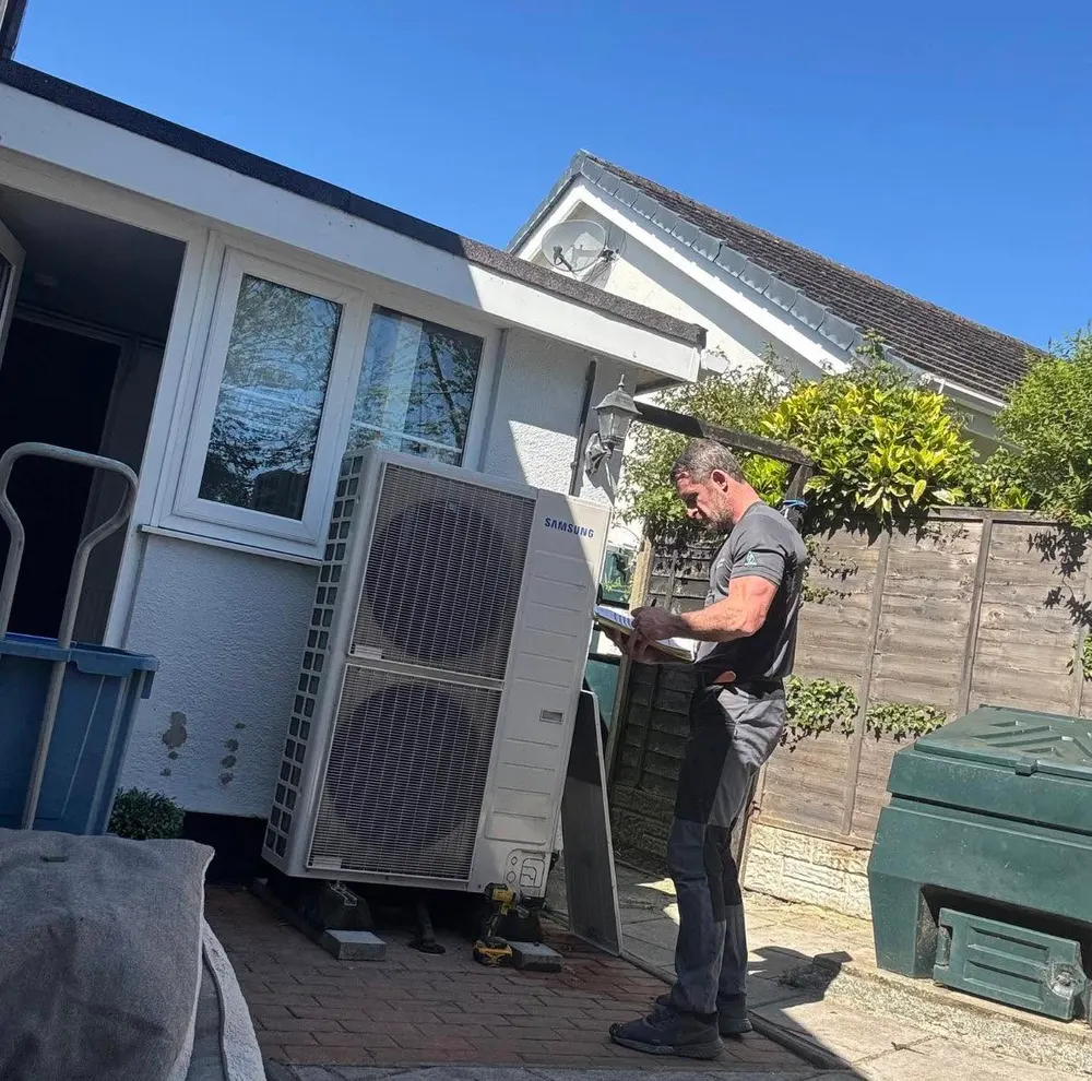 Engineer filling in commissioning paperwork beside a Samsung outdoor heat pump unit