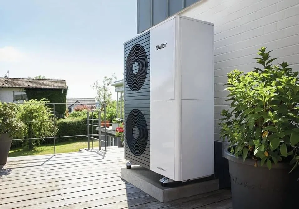 Air source heat pump installed on a raised base beside a house