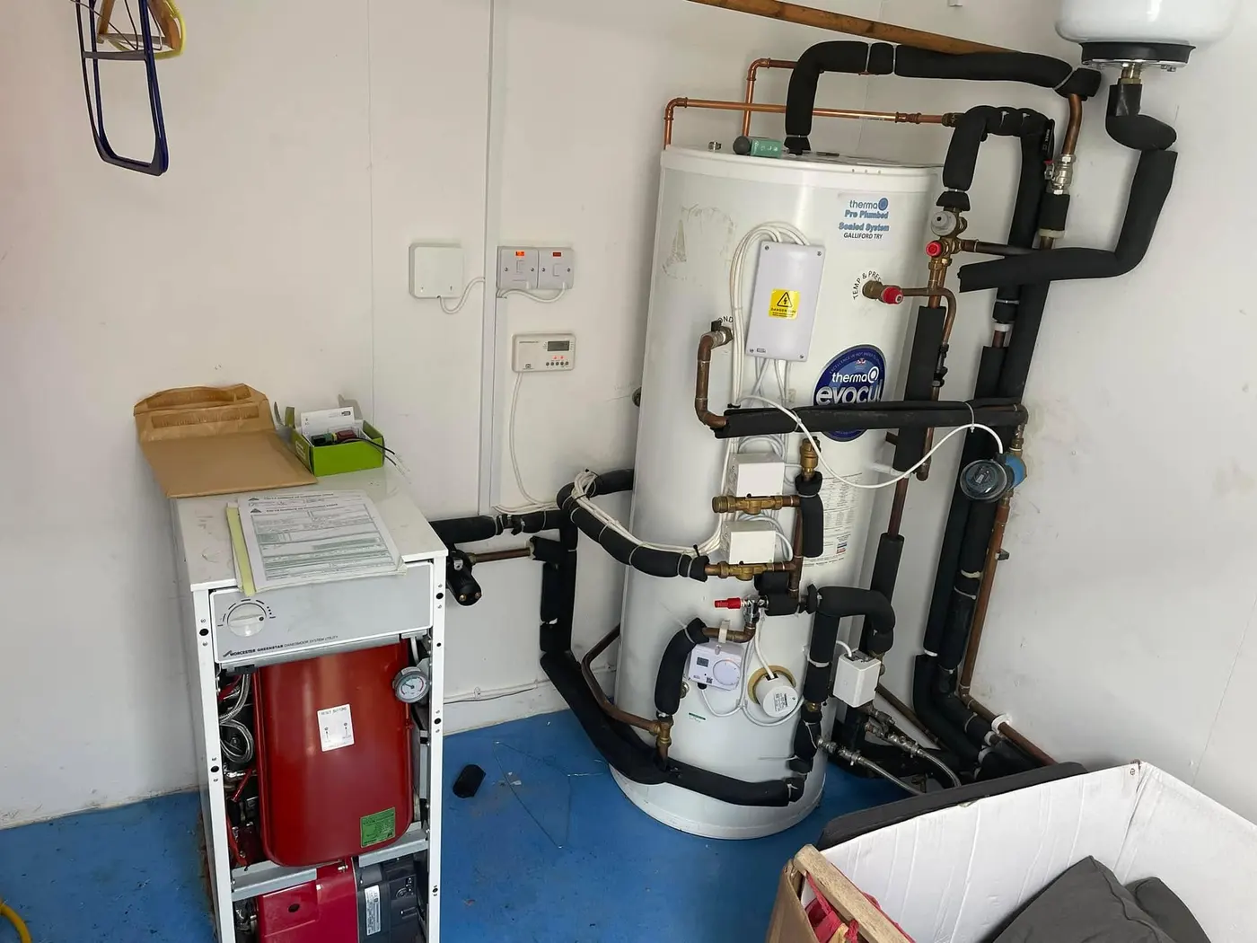 Floor-standing oil boiler next to a new unvented hot water cylinder with insulated pipework
