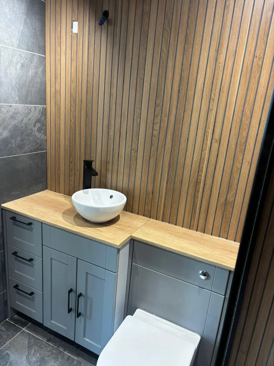 Grey vanity unit with oak worktop, countertop basin and black tap against wood slat panelling
